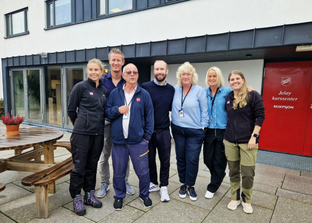 Fire kvinner og tre menn står samlet utenfor et bygg med rød dør. På den er logoen til Frelsesarmeen og under står det med hvit skrift "Jeløy kurssenter resepsjon".r