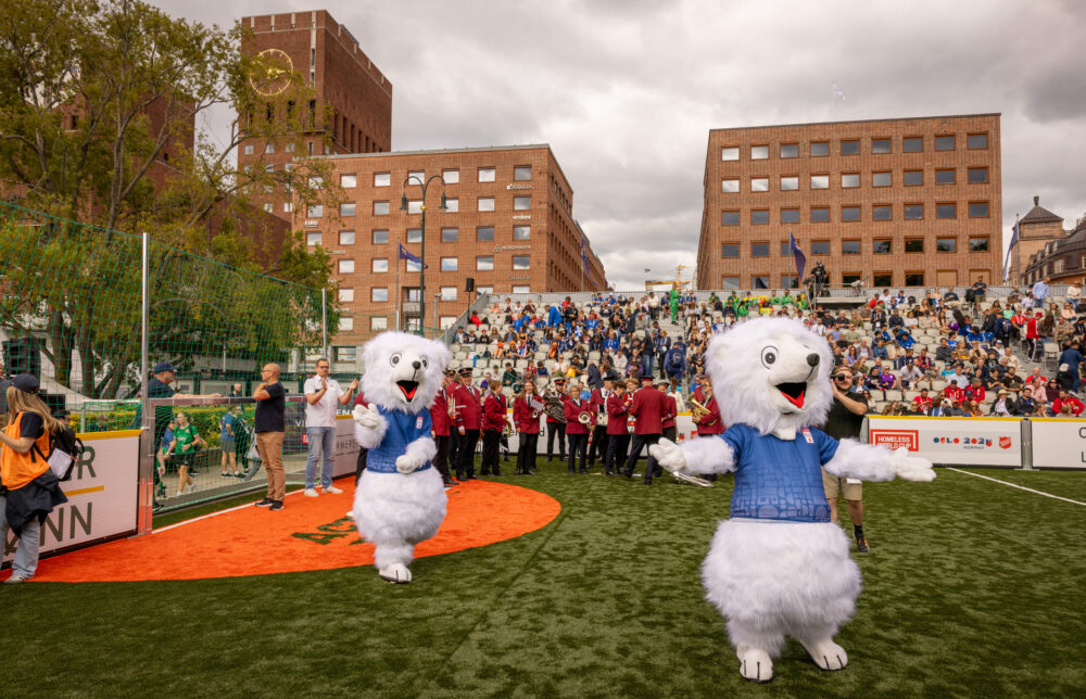 Foto: To hvite isbjørn-maskoter løper rundt på en liten fotballbane. Tribunene er fulle av folk og i bakgrunnen sees Rådhuset i Oslo.