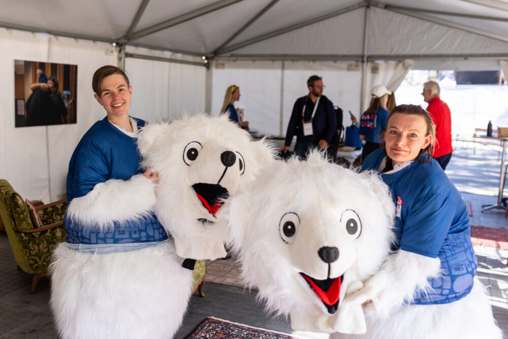 Foto: To kvinner i isbjørndrakt står med hver sitt store, maskehode i armene. De ser glade ut. I bakgrunnen i det store teltet står noen mennesker.