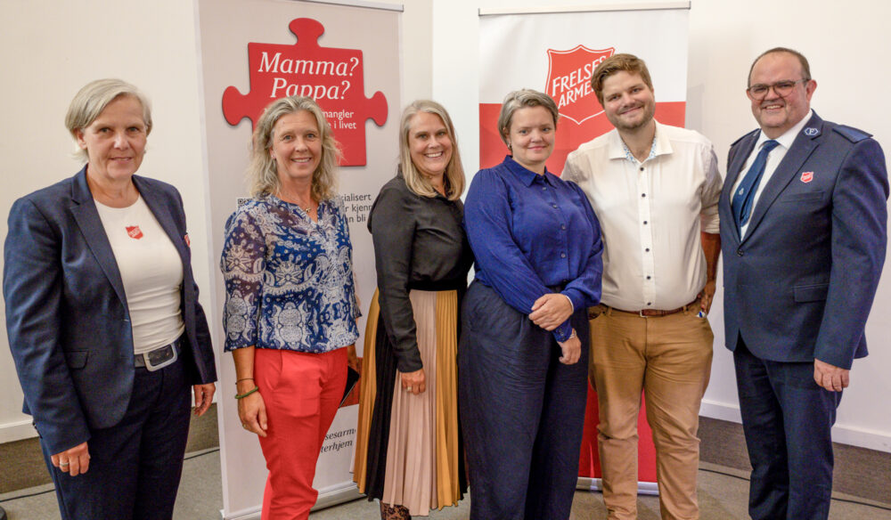 Foto: Foran to toll-ups om Frelsesarmeens fosterhjem står seks personer, fire kvinner og to menn. De to på hver flanke har på seg uniform fra Frelsesarmeen.