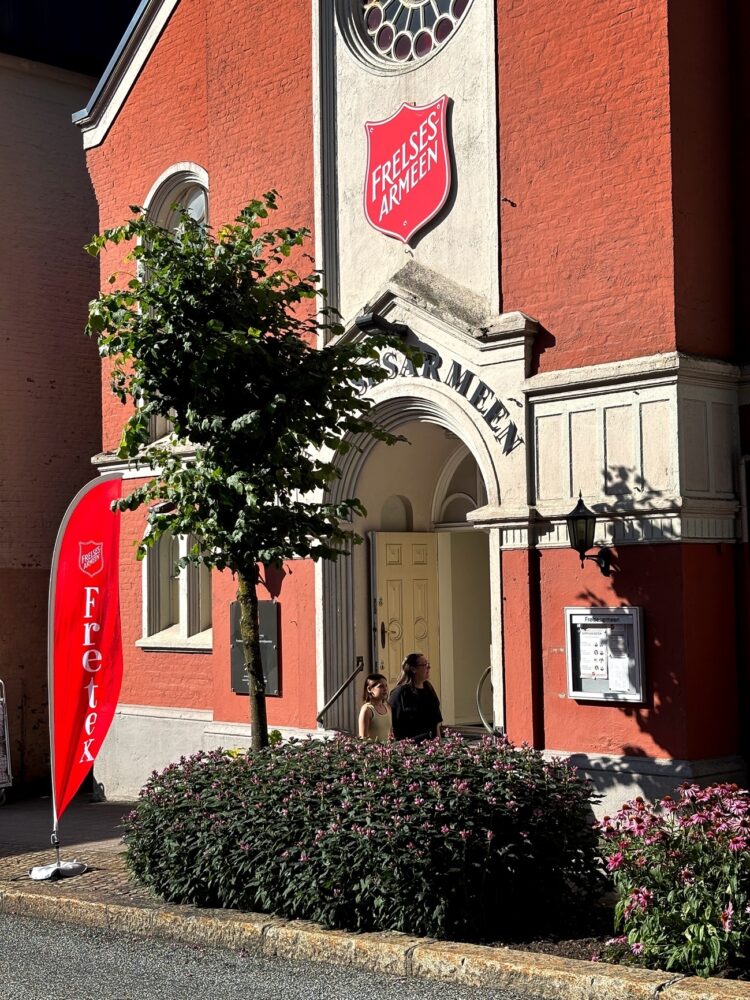 Foto: Eksteriør av kirkelignende murbygg i lakserødt og beige med stor logo fra Frelsesarmeen.