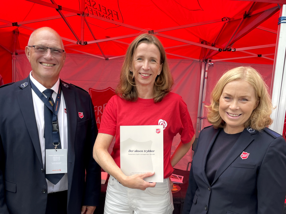 Foto: Mann og to kvinner står på en rekke i et telt. Hun i midten har på seg rød T-skjorte, de andre to er i uniform fra Frelsesarmeen.