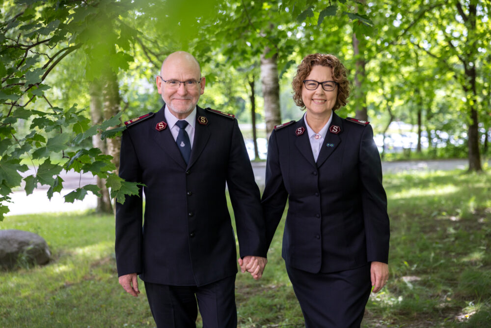 Foto: Ektepar i uniformer fra Frelsesarmeen går i en grønn skog. Begge har briller og holder hender.