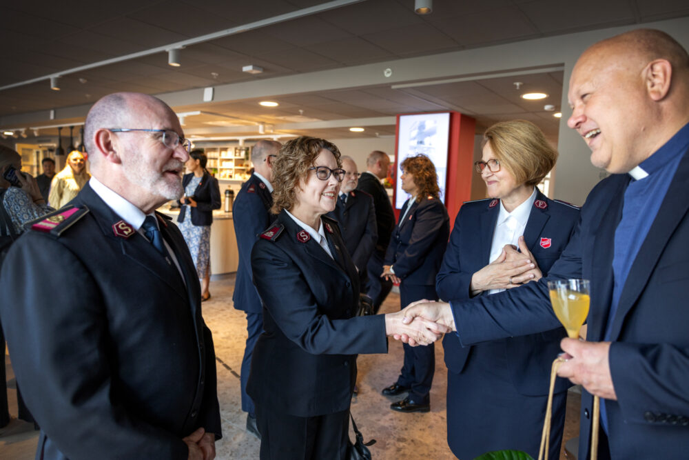 Foto: Mann med blå prestesnipp står ved tre personer i uniform fra Frelsesarmen. Han hilser på den ene kvinnen.