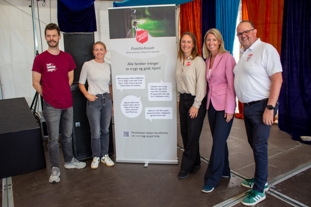 Foto: To menn og tre kvinner står foran en roll-up inne i teltet. Den har logoen til Frelsesarmeen på og har snakkebobler med sitater fra barn.