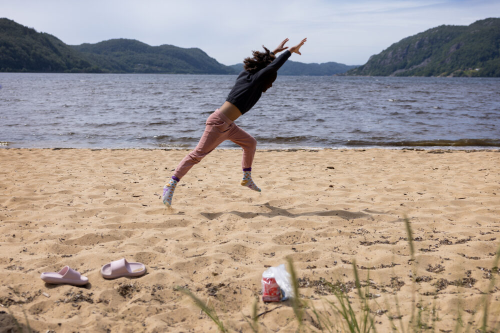 To foto: Først ei jente i småskolealder som slår hjul i sanden like ved sjøen. Deretter nærbilde av de prikkete strømpene hennes i rosa strandtøfler.