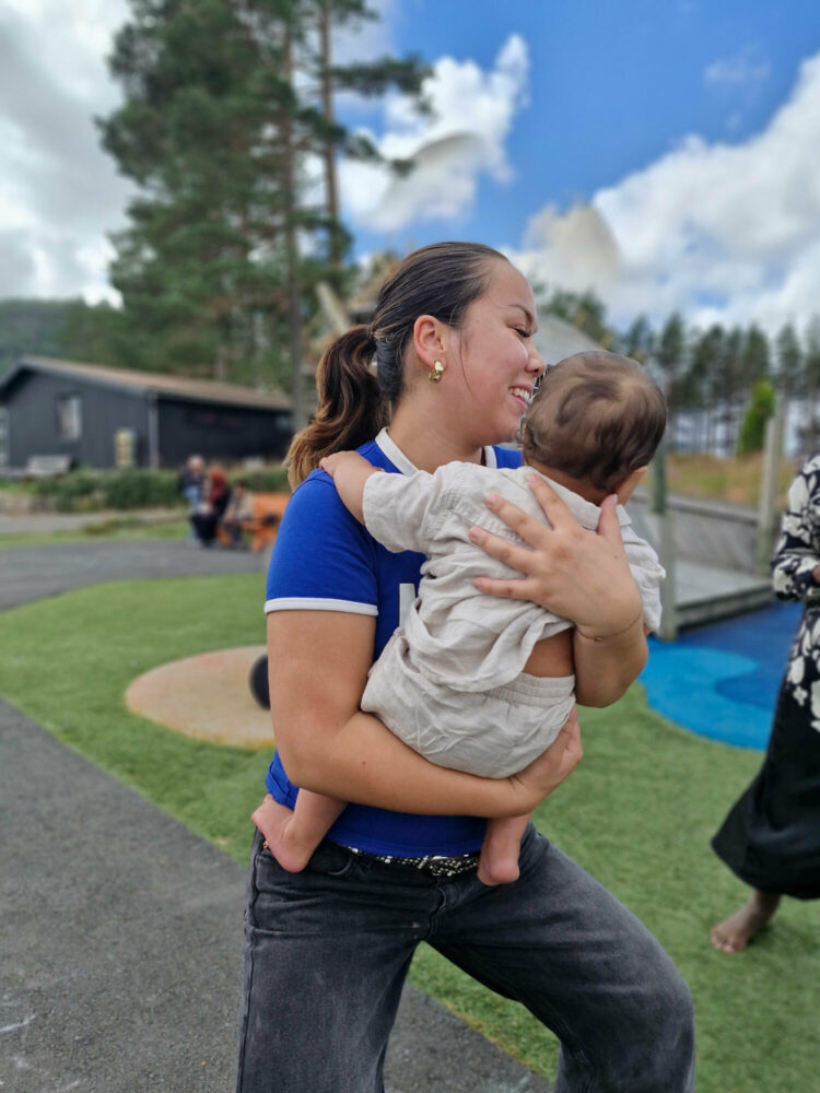 Foto: På en lekeplass bærer en tenåringsjente en baby på et halvt år på armen.