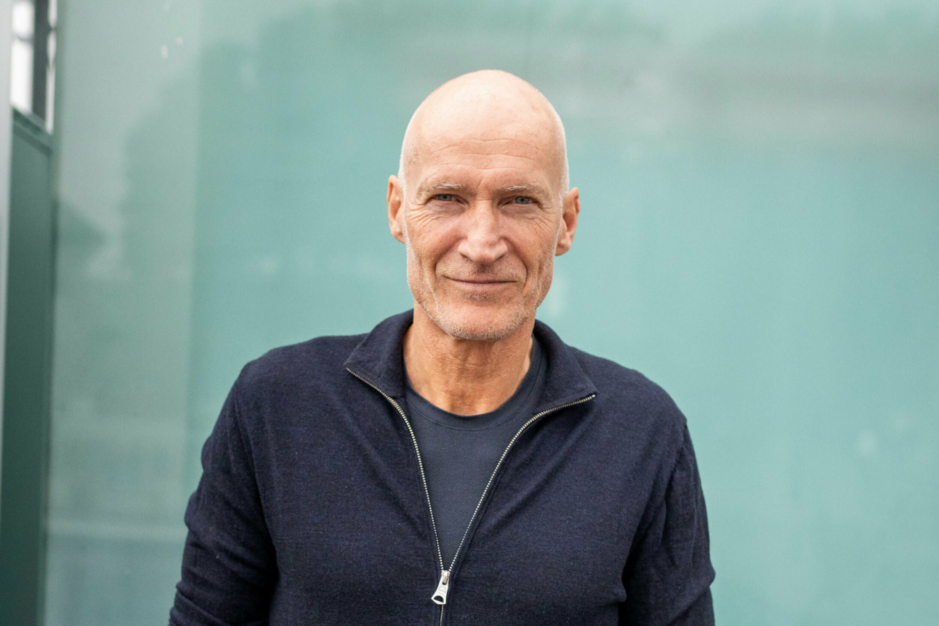 Foto: Mann tidlig i 60-årene med blank isse står foran en grønn glassdør.