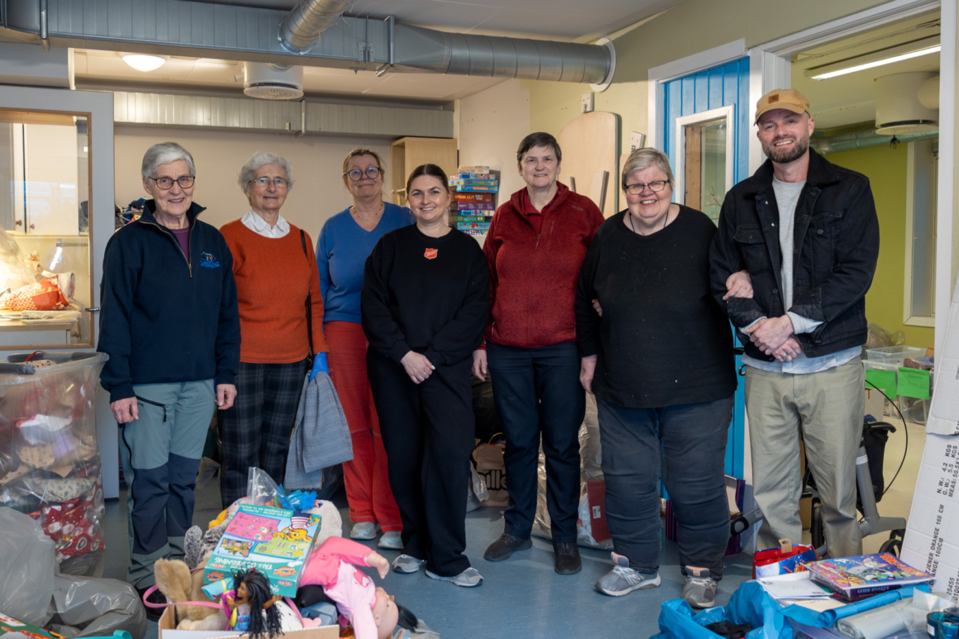 Foto: Seks kvinner og én mann står oppstilt på rekke. Rundt dem ligger det utpakkede gaver i forskjellige stabler.