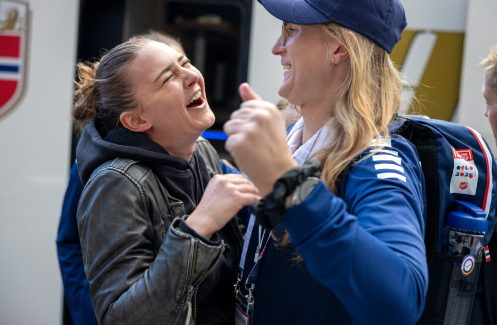 Foto: To spillere på det norske damelaget som ler og skal til å gi hverandre en klem. De er nettopp kommet av en buss.