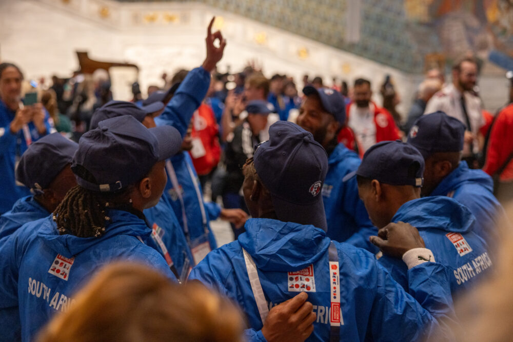 Foto: Glade mennesker i kongeblå drakter står i ring og holder rundt hverandre. Det står Sør-Afrika på ryggen.