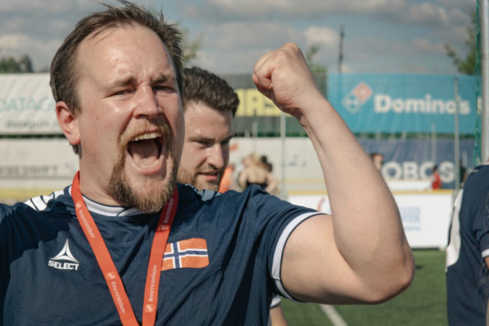 Jublende mann med skjegg på en fotballbane, med en knyttet hånd i været.