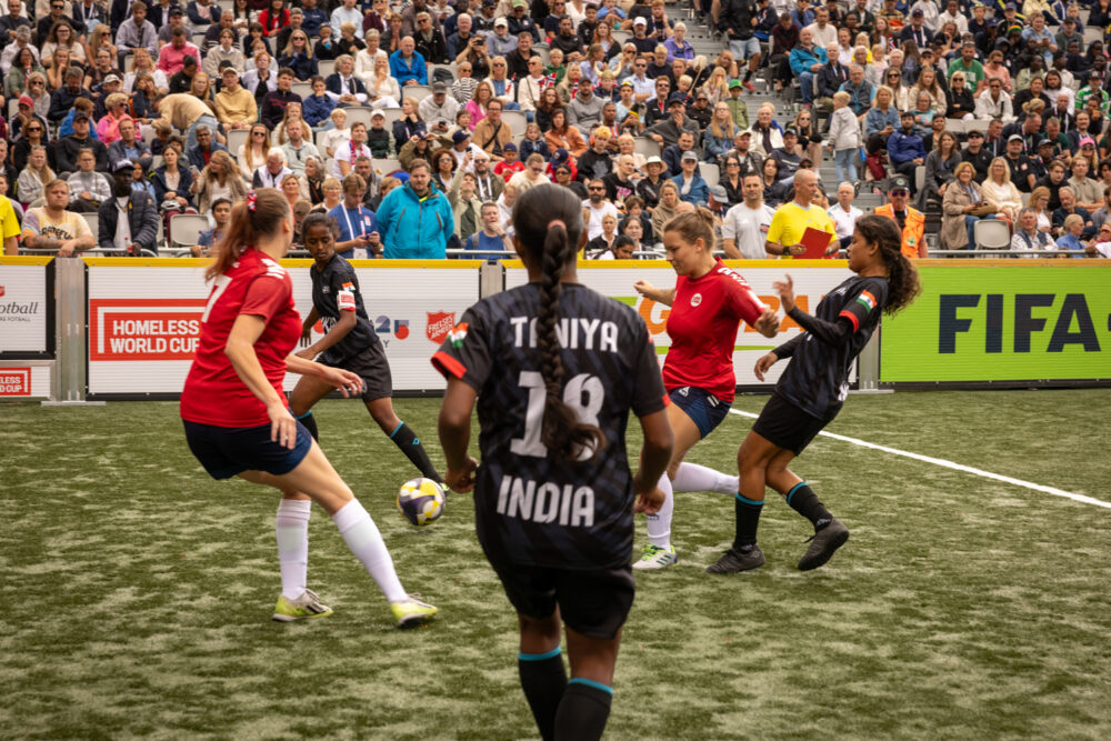 Foto: Kvinner i røde og svarte drakter kjemper om en fotball.