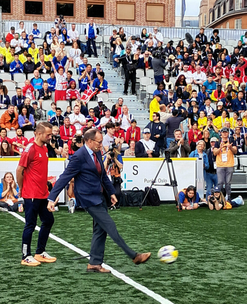 Foto: Mann i 50-årene i dress med litt lite, mørkt hår opå toppen og briller. Han sparker en ball i fart.