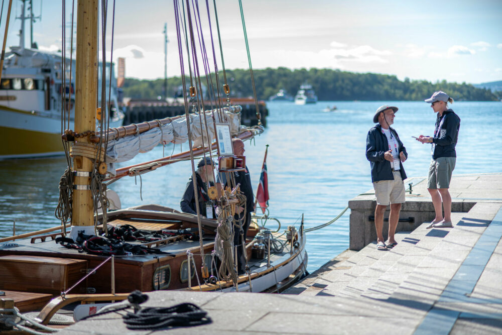 Foto: Seilbåt ligger til kai. Der står en mann med hatt og en kvinne med caps mot hverandre.