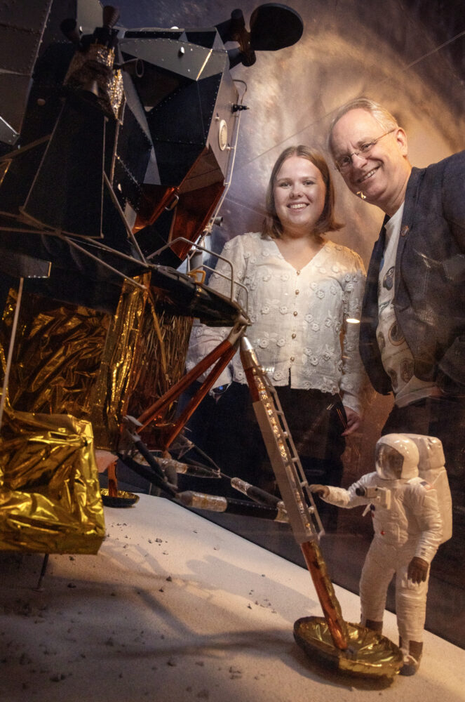 Foto: Voksen mann og ung kvinne ser gjennom glasset på en monter inn på en utstilling av en liten astronaut som skal til å klatre opp en stige.