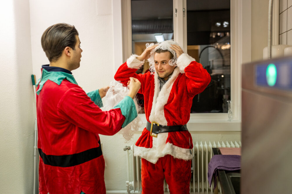 Foto: Her har de fått på seg draktene og han som er nissen smiler mens han drar på seg en hvit parykk med krøller.