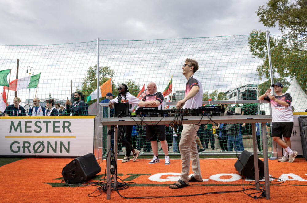 Foto: Mann ved miksepult ser utover publikum. På hver sin side av ham står to andre menn i lik T-skjorte.