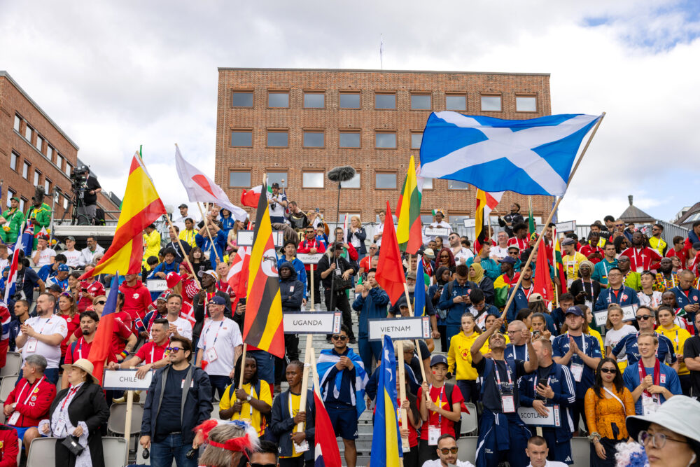 Foto: Tribune full av flagg fra mange ulike land. Bak ser man røde mursteinsbygninger.