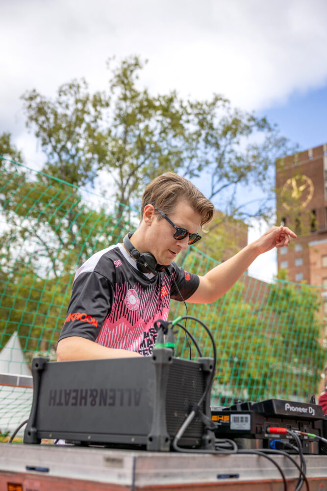 Foto: Mann med solbriller står ved en miksepult. I bakgrunnen sees grønne trær og klokka på det ene tårnet i Oslo rådhus.