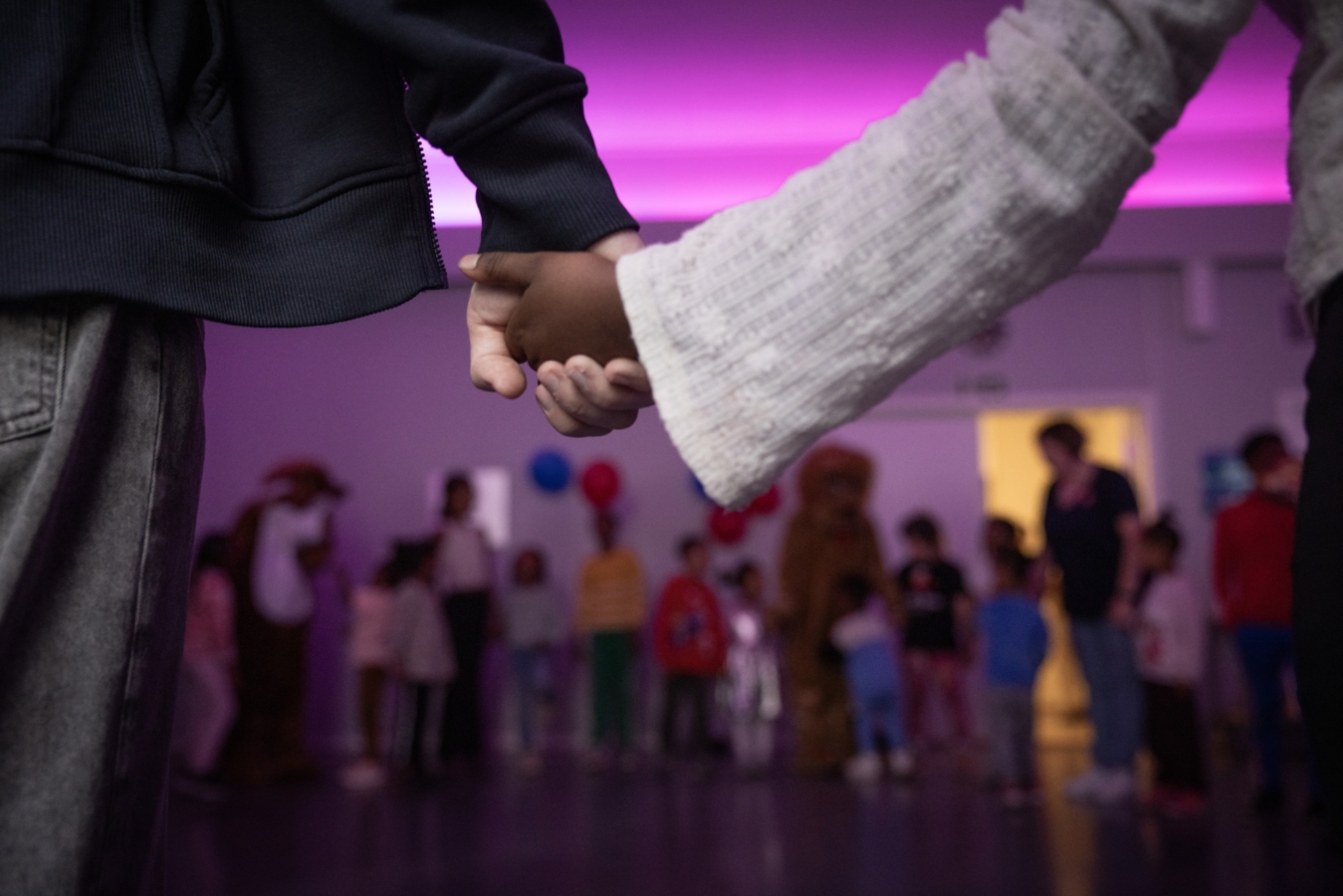 Foto: Barn som holder hender. De står i en ring i et stort rom med mange andre.