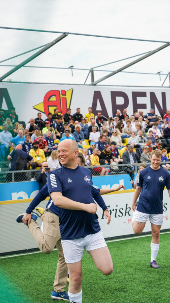 Foto: Oppvarming av tre fotballspillere, der Vedum står i midten i hvit T-skjorte og hvit shorts. Han smiler bredt.