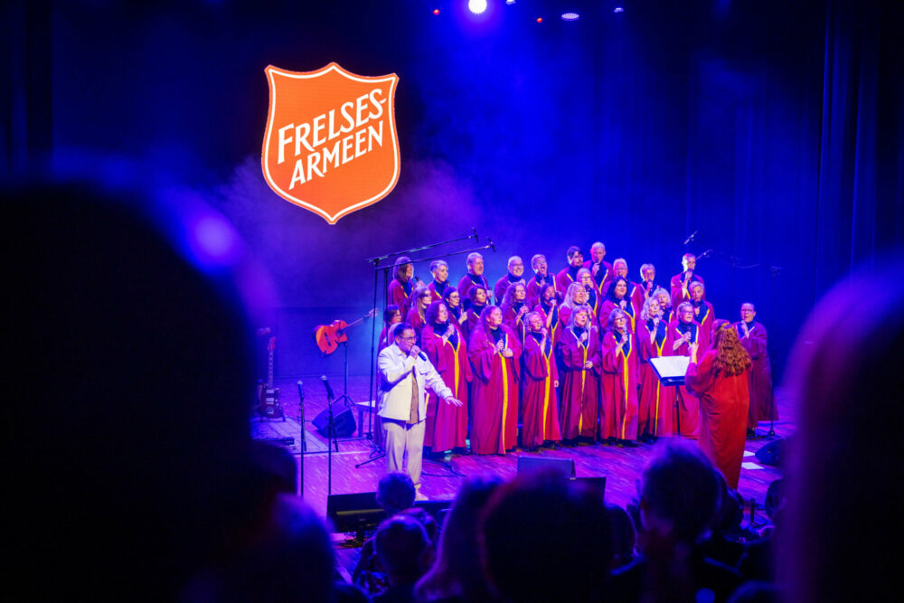 Foto: Kor i røde kapper på scene med blått lys. Til venstre står solisten.