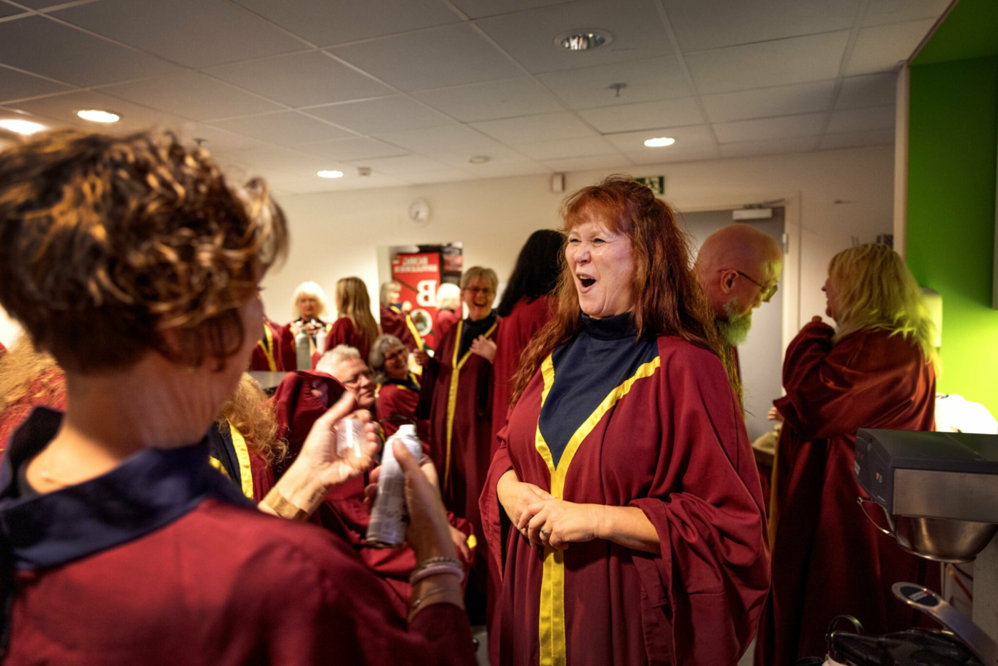 Foto: En gjeng med korsangere i kapper står og sitter på et bakrom.