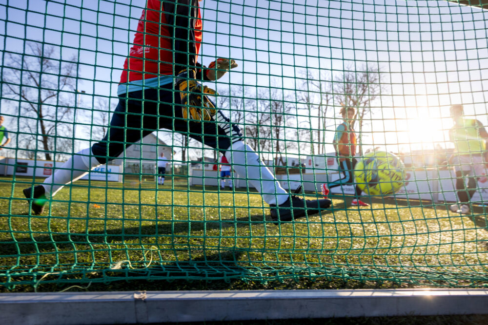 Foto: Flere fotballspillere sees gjennom nettingen på det lille målet. Banen er også liten.