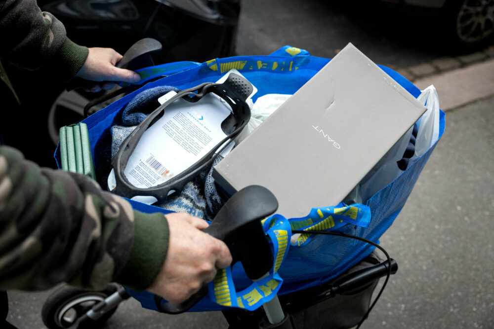 Foto: Hender som kjører en rullator på gata. Den er lesset med en blå KEA-bag full av ting.