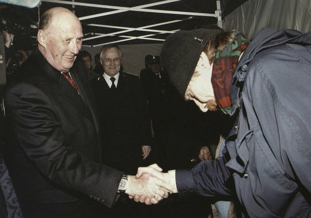 Foto: En mann med lue og skjerf bukker dypt når han hilser på en eldre mann i svart jakke og slips inne i et telt.