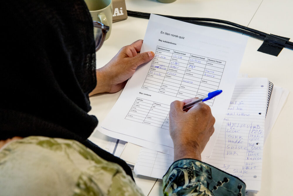 oto: Nærbilde av en kvinne som skriver på et oppgaveark. Bare arket, hendene og baksiden av hodet synes.