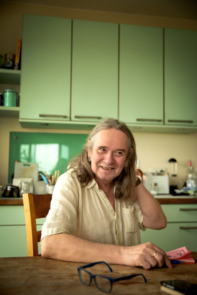 Foto: Mann med halvlangt, brunt hår sitter ved kjøkkenbordet. I bakgrunnen sees kjøkkeninnredningen som er mintfarget.