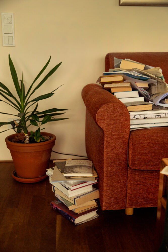 Foto: Rød sofa med mange  bøker opp og en stabel vd siden av.