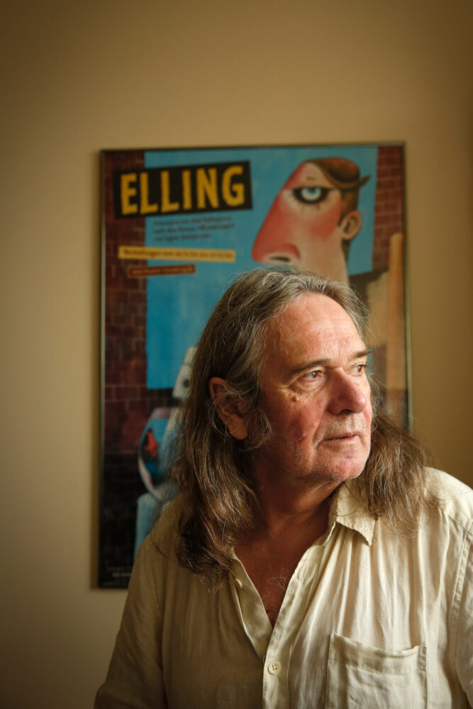 Foto: Mann med halvlangt hår og beige skjorte. Ser bort mor noe. I bakgrunnen henger en kunstplakat der det står Elling med store bokstaver.