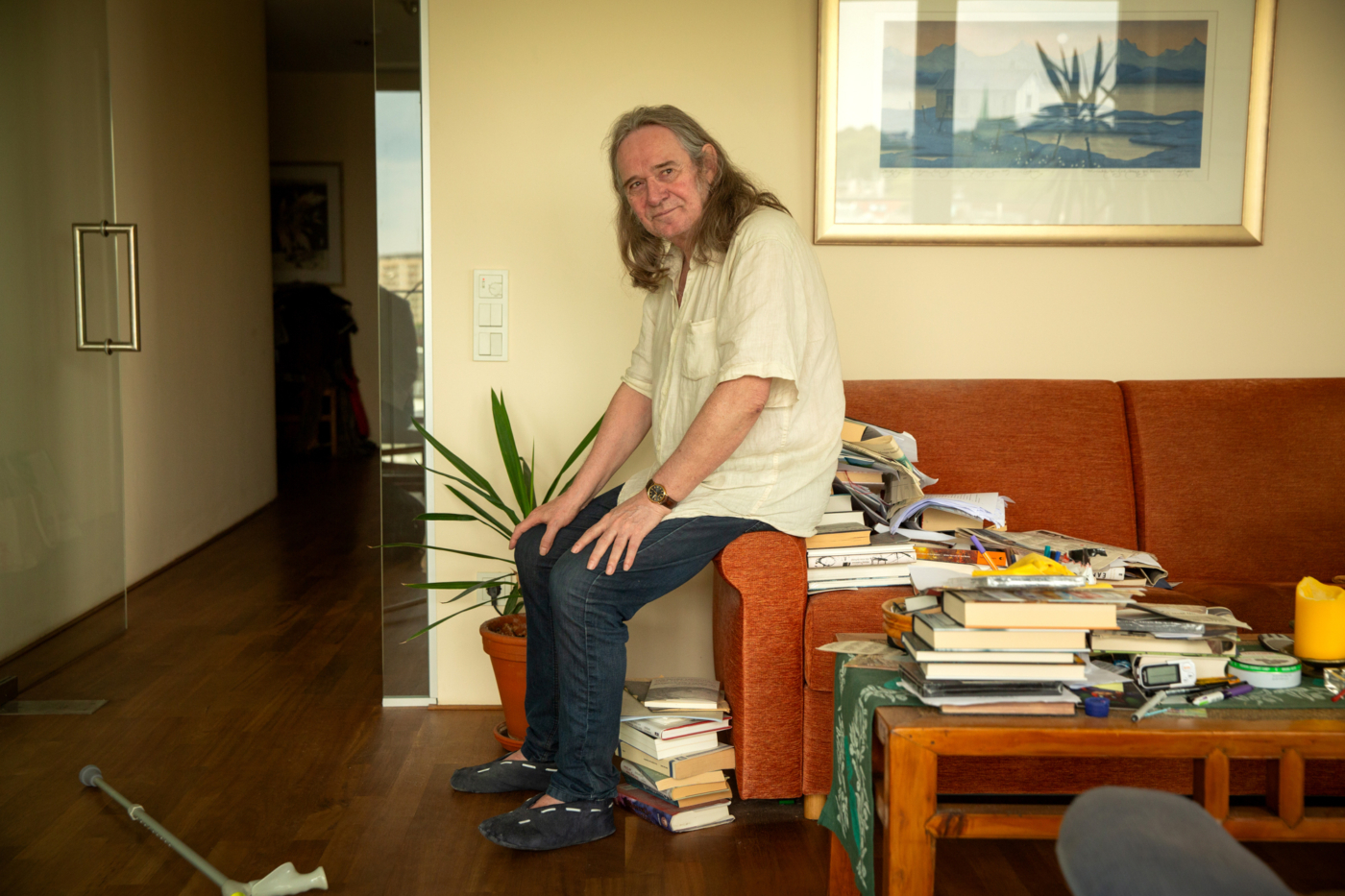 Foto: Mann med halvlangt hår sitter på armlenet til en rød sofa. Der ligger det bøker over alt.