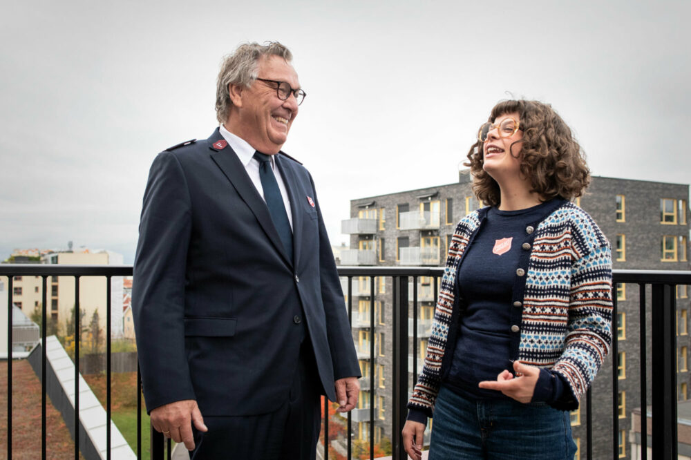 Foto: Eldre herre i uniform fra Frelsesarmeen står sammen med en ung jente med mørkt, krøllete hår. Begge har briller og står på en terrasse høyt hevet over Oslo.