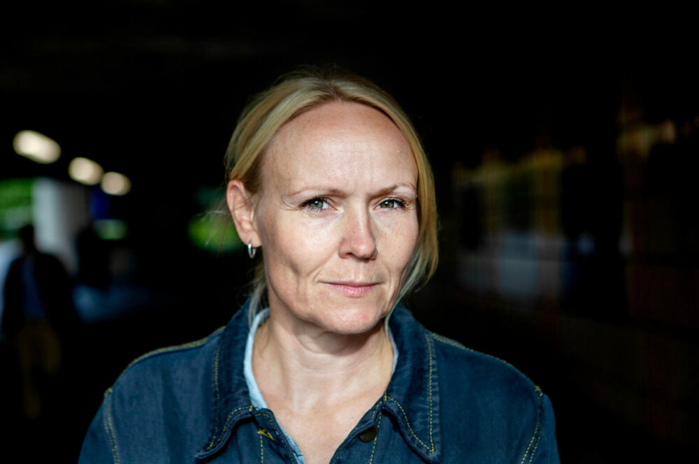 Foto: Nærbilde av en blond kvinne i dongerijakke. Det er blitt mørkt ute.