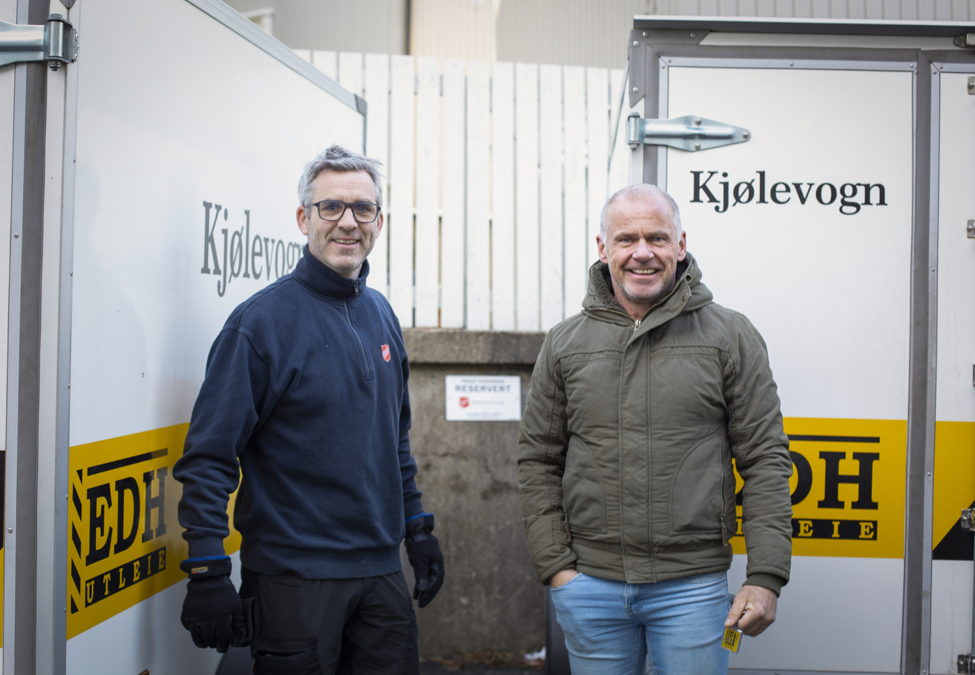 Foto: To menn står ute mellom to kjølevogner.