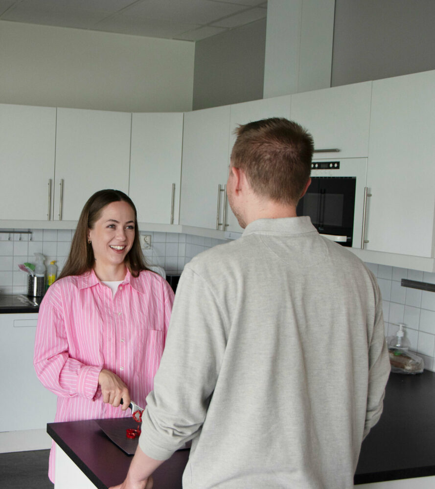Foto: Kvinne med mørkt, langt hår i rosa skjorte står på et kjøkken og skjærer opp grønnsaker mens hun snakker med en ung gutt med ryggen til. Han har på seg en lys beige genser.