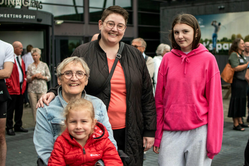 Foto: To kvinner og to jenter foran et bygg med flere mennesker utenfor. Den eldste er mormor og mor til de andre tre.