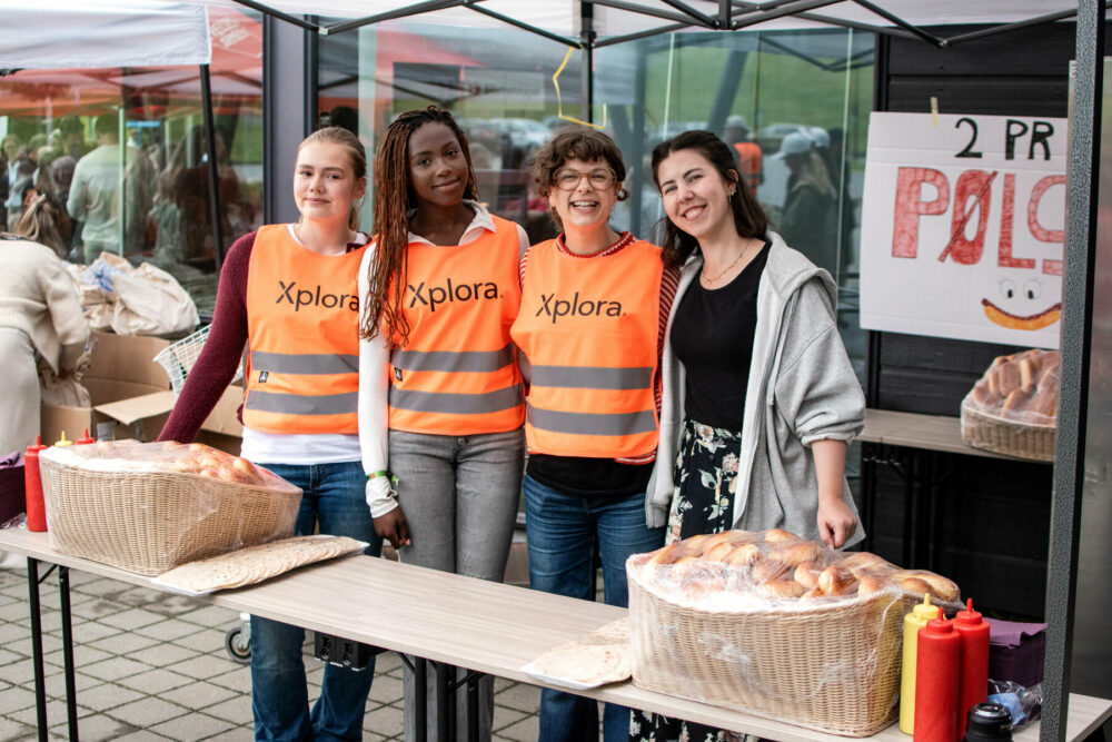 Foto: Fire unge kvinner på rekke foran et bord der de skal servere. Tre av dem har på seg oransje vester.