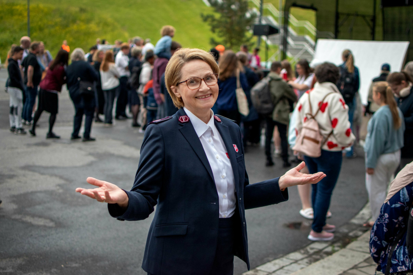 Foto: Kvinne i 60-årene med bob-klipp og briller. Hun har på seg uniform fra Frelsesarmeen og holder ut hendene.