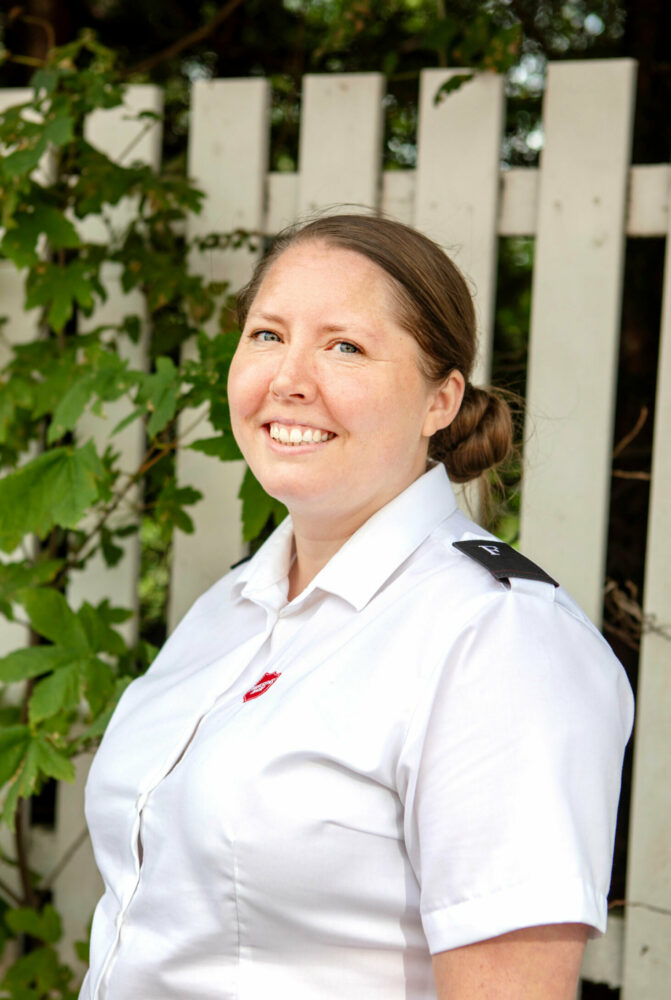 Foto: Kvinne i slutten av 30-årene med langt, mørkeblondt hår oppsatt i en knute. Hun står ute og har på seg en hvit skjorte fra Frelsesarmeen.