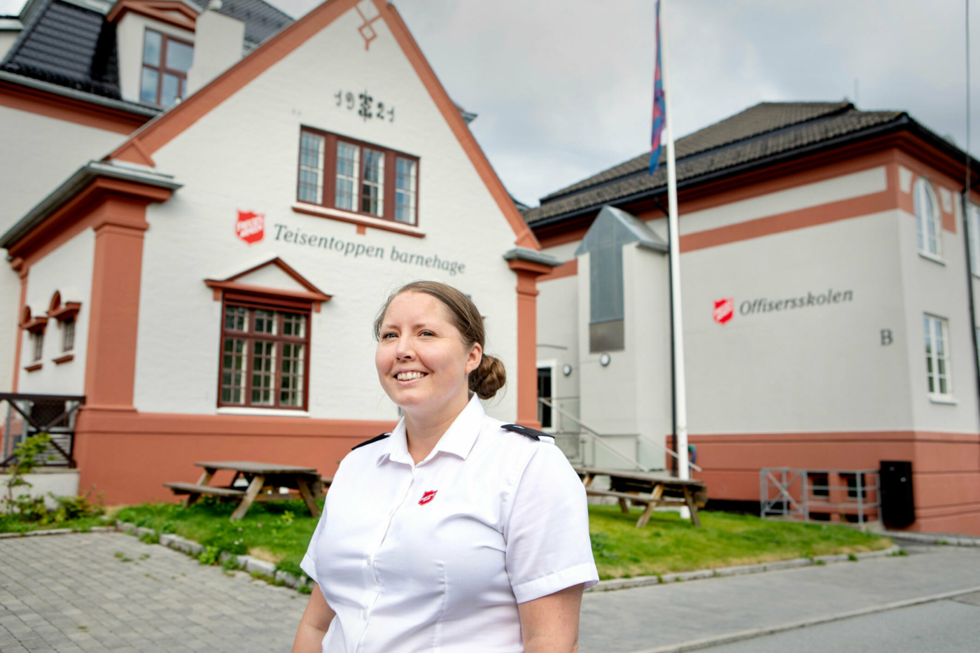 Foto: Kvinne i slutten av 30-årene står i hvit uniformsskjorte foran et bygg som tilhører Frelsesarmeen.