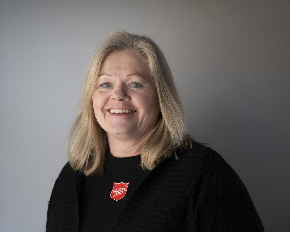 Foto: Kvinne med blondt hår i svart genser med rød logo fra Frelsesarmeen.