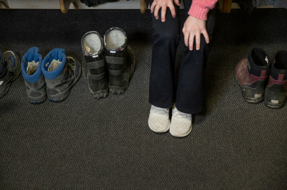 Foto: Hendene til et barn som tar på seg sko i en garderobe.
