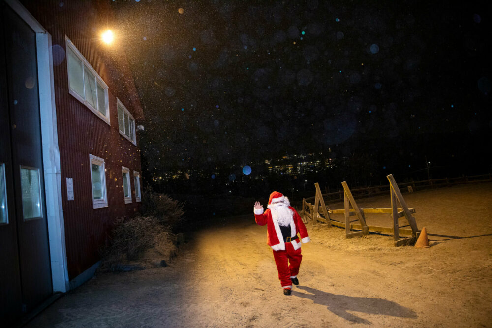 Foto: Mann i nissedrakt kommer gående langs et rødt hus i snøen.