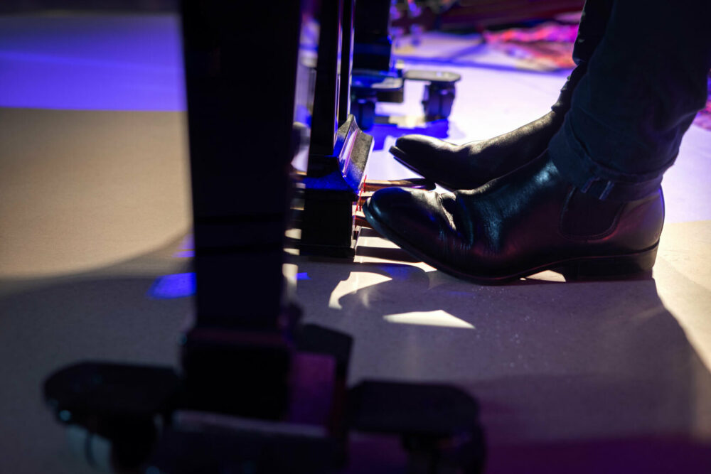 Foto: Føtter i blanke, svarte sko som tråkker på pedalene under pianoet.