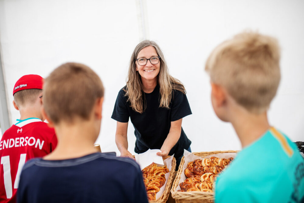 Undervisningssituasjon. Læreren midt mellom ungene som man ser rygg og bakhodene til.